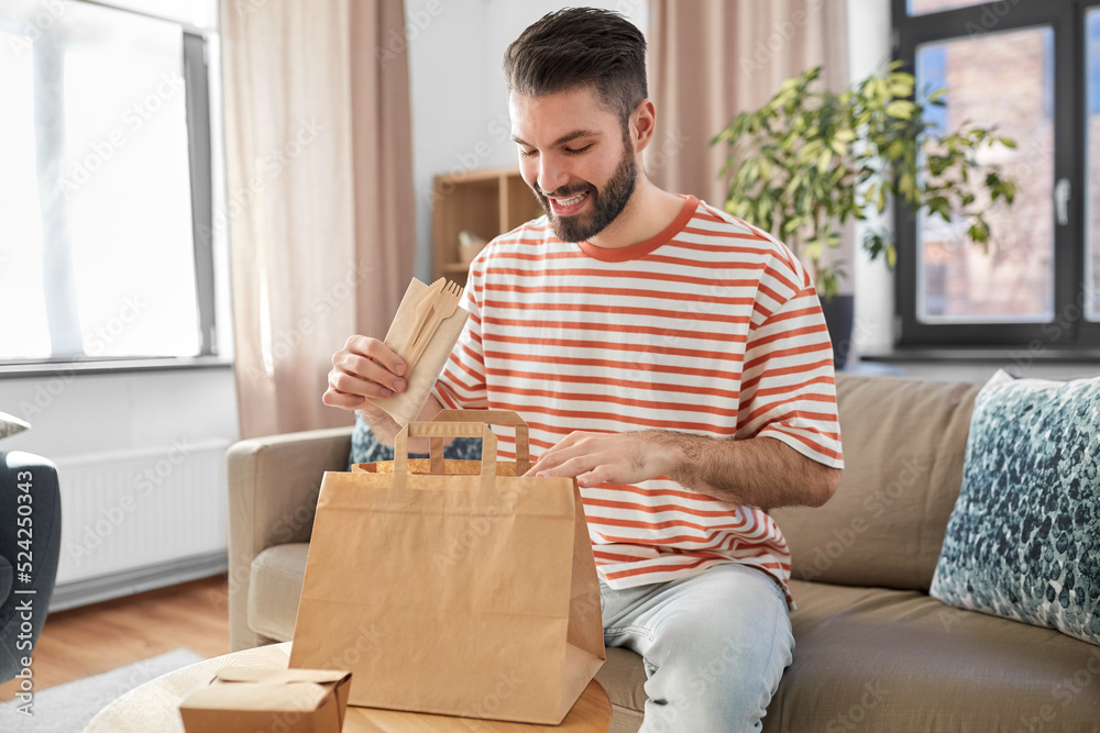 consumption, eating and people concept - smiling man unpacking takeaway food in paper bag at home consumption, eating and people concept - smiling man unpacking takeaway food in paper bag at home