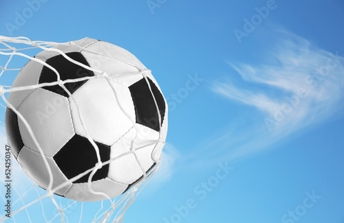 Soccer ball in net against blue sky