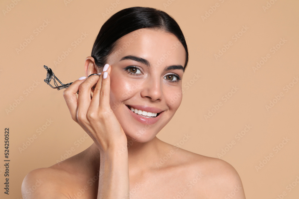 Beautiful young woman with eyelash curler on beige background Beautiful young woman with eyelash curler on beige background
