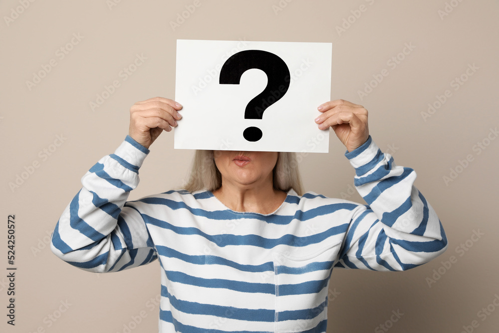 Mature woman holding paper with question mark on beige background Mature woman holding paper with question mark on beige background