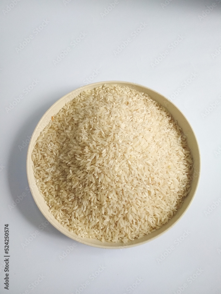 A plate of white raw rice, on a white background top view A plate of white raw rice, on a white background top view