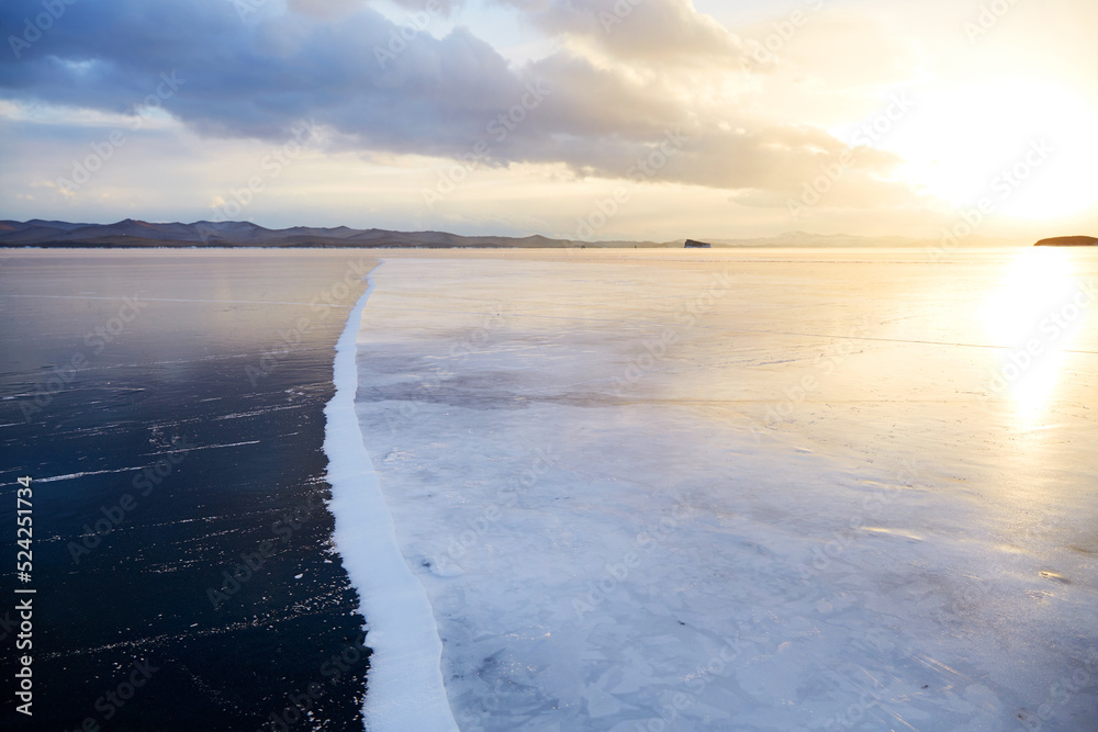 Beautiful sunset on the frozen Lake Baikal. Pure transparent ice and white ice with snow. Winter landscape