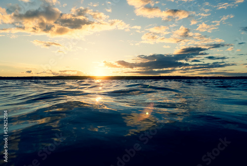 Water surface. View of a Sunset sky background. Dramatic gold sunset sky with evening sky clouds over the lake. Clear water texture. Landscape. Water reflection