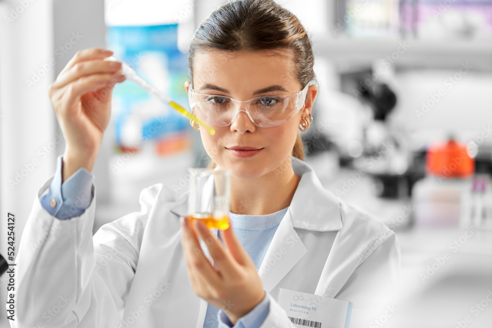 science research, work and people concept - female scientist in goggles with dropper and chemical or test sample in beaker working in laboratory science research, work and people concept - female scientist in goggles with dropper and chemical or test sample in beaker working in laboratory