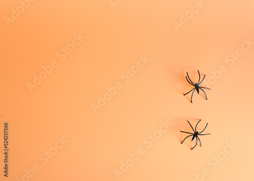 Two small artificial spiders with long legs on a orange background. Creative halloween concept backdrop. halloween craft.