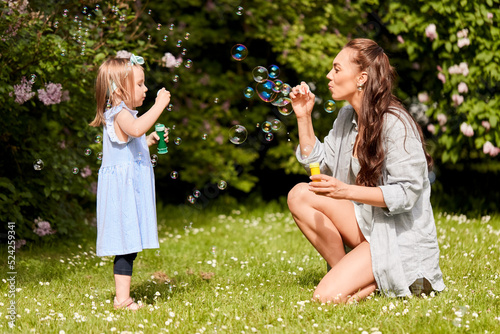 family  motherhood and people concept - happy mother with little daughter blowing soap bubbles at summer park or garden