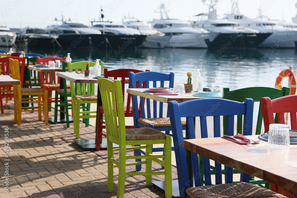 Beautiful view of outdoor cafe with colorful wooden chairs near pier