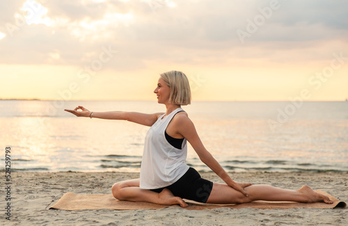 fitness, sport, and healthy lifestyle concept - woman doing yoga pigeon pose on beach over sunset