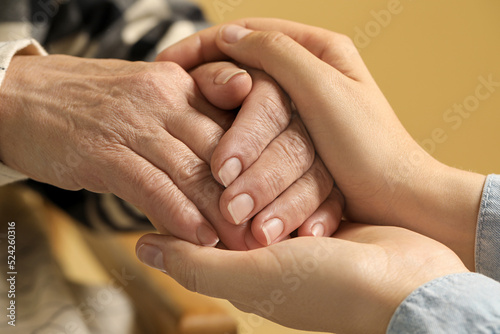 Fototapeta Naklejka Na Ścianę i Meble -  Young and elderly women holding hands on beige background, closeup