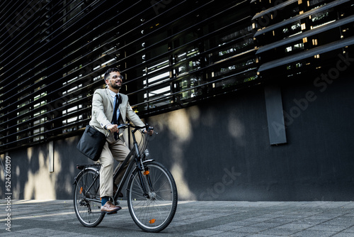 Fototapeta Businessman riding bicycle in front of modern office building.