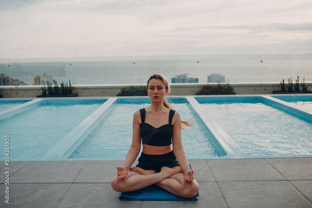 Caucasian woman practicing yoga at swimming pool and cloudy sky