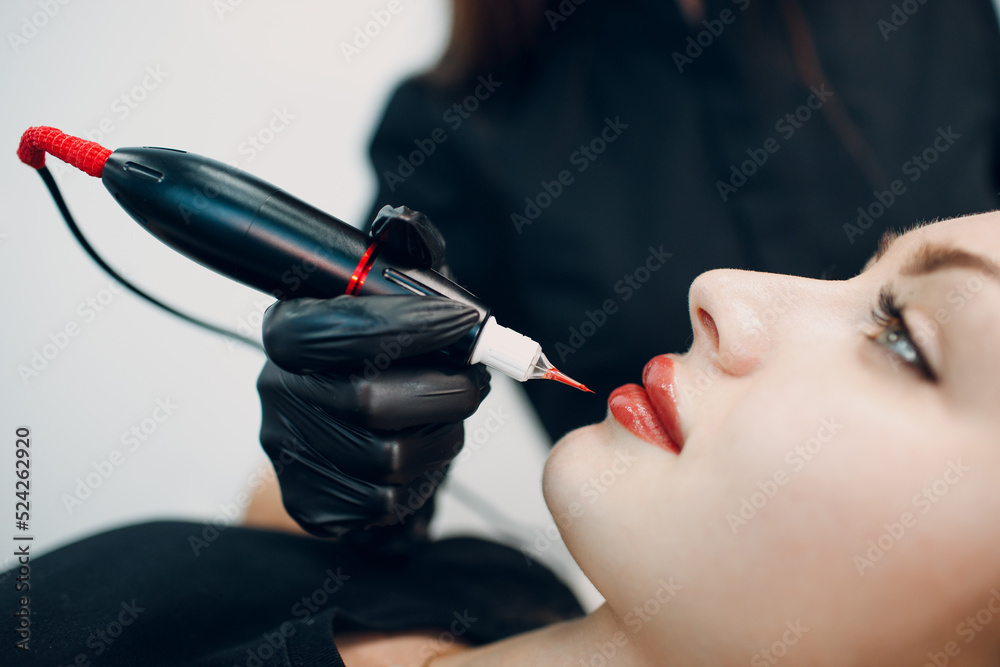 Cosmetologist applying red permanent make up tattoo on female lips. - obrazy, fototapety, plakaty 