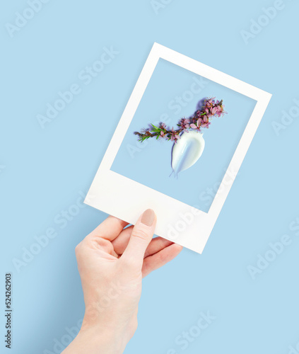Creative concept photo of hand with polaroid picture with flowers on blue background.