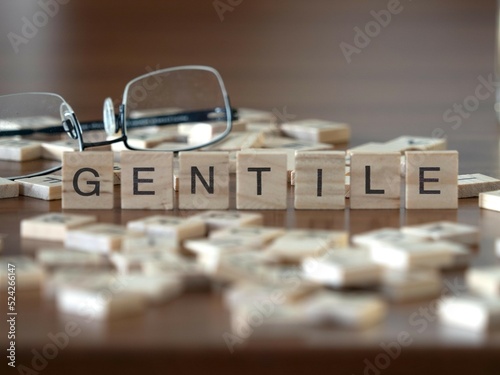 gentile parola o concetto rappresentato da piastrelle di legno su un tavolo di legno con occhiali e un libro photo