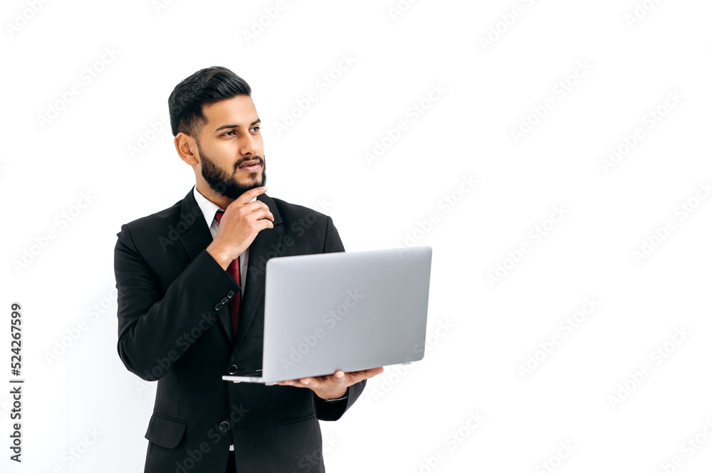 Puzzled thoughtful elegant influential arabian or indian man in formal suit, stand on isolated white background with laptop, pensively looking away, thinking, dreaming.Copy-space for your presentation Puzzled thoughtful elegant influential arabian or indian man in formal suit, stand on isolated white background with laptop, pensively looking away, thinking, dreaming.Copy-space for your presentation