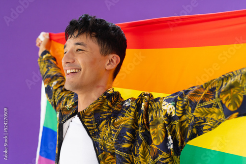Happy biracial man holding lgbt rainbow flag and smiling on purple background