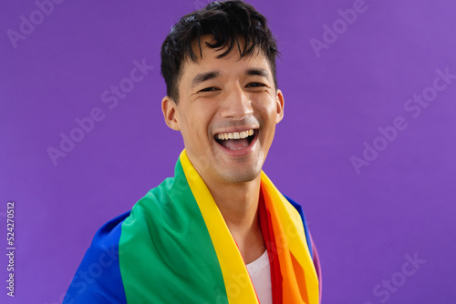 Portrait of happy biracial man holding lgbt rainbow flag and smiling on purple background