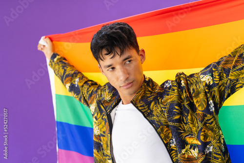 Happy biracial man holding lgbt rainbow flag and smiling on purple background