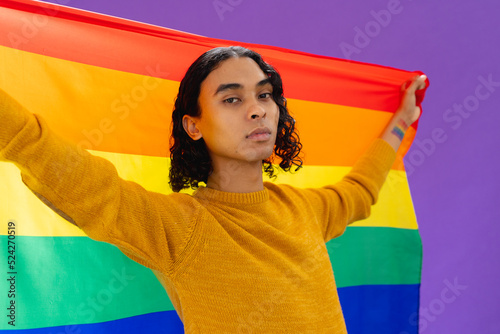 Portrait of happy biracial man holding lgbt rainbow flag on purple background