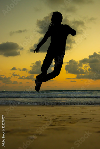A girl jumping on the beach over the sands  orange horizon with clouds  waves  black shadow object