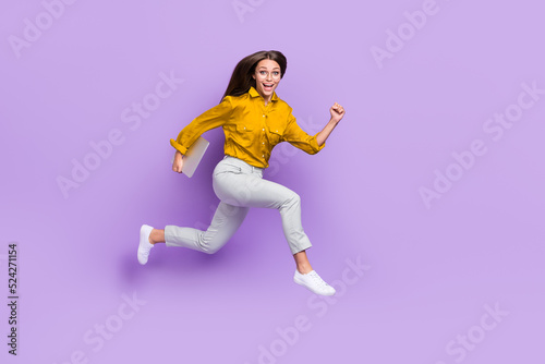 Full length profile photo of active carefree person hold netbook rush jump isolated on violet color background