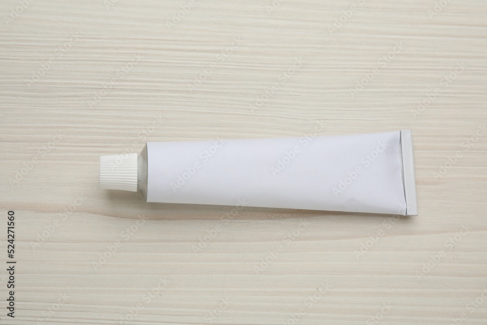 Fototapeta premium Blank white tube of ointment on light wooden table, top view. Space for text