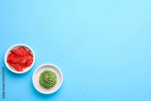 Bowls with swirl of wasabi paste and pickled ginger on light blue background, flat lay. Space for text photo