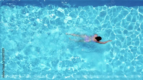 Close up, top view of a young caucasian woman, swimming relaxed in a crystal clear pool. Concept holidays, travel, summer, 4k resolution.