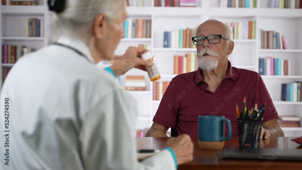 Obraz premium Mature senior male doctor discussing treatment with prescription drug to female patient in modern clinic with books background.