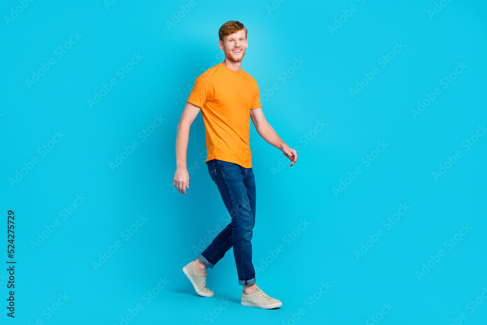Full size profile photo of cheerful ginger hair guy go wear t-shirt jeans shoes isolated on blue color background Full size profile photo of cheerful ginger hair guy go wear t-shirt jeans shoes isolated on blue color background