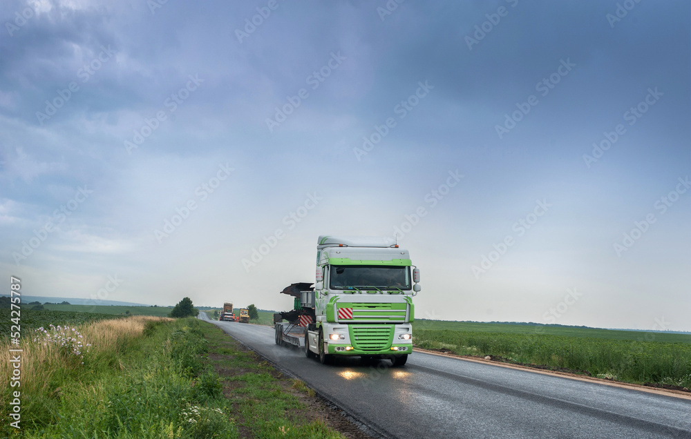 a big truck driving on a rainy wet highway around fields with headlights reflecting on the road, beautiful scenery with storm clouds