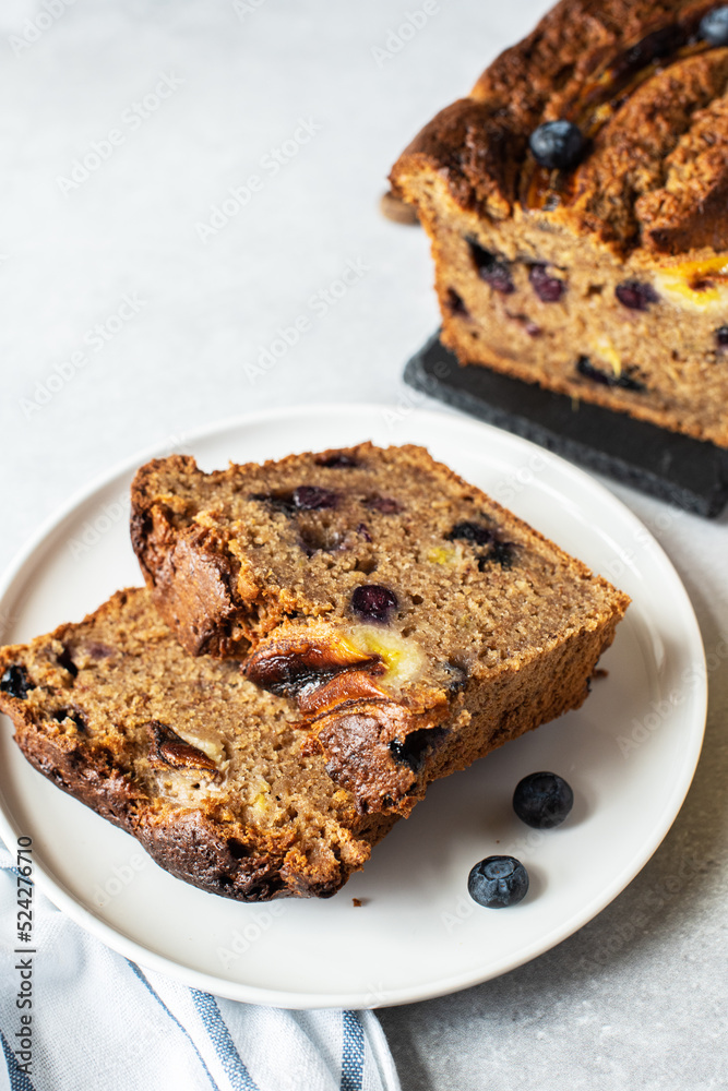 Slices of banana bread with blueberries served on a plate on a gray background.