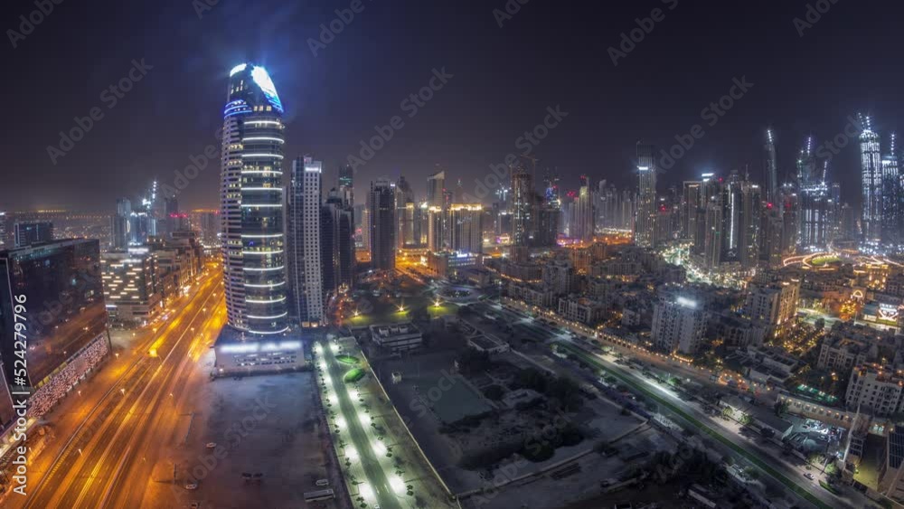 Panorama of Dubai's business bay and downtown towers during all night aerial timelapse. Rooftop view of some skyscrapers and new towers under construction and moon on the sky