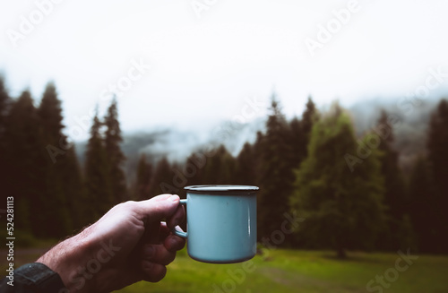 Blue cup in hands with forest background. Cinematic travel inspirational background
