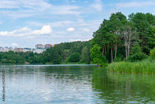Panorama of Zhytomyr, a forest with a river against the backdrop of residential buildings in the distance.