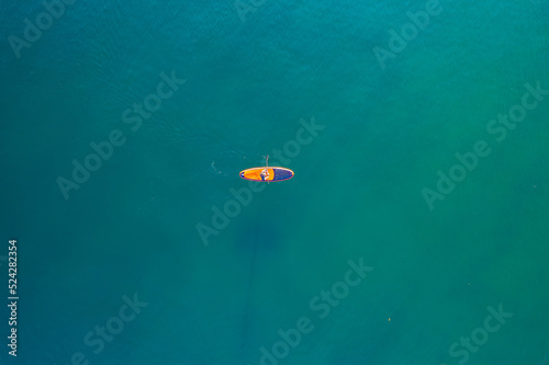 Man rowing oar on sup board blue sea water. Aerial top view paddleboard