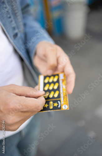 Istanbul, Turkey- 09.10.2022:  A man hand scratching turkish lottery card with coin. The focus is on his hand.