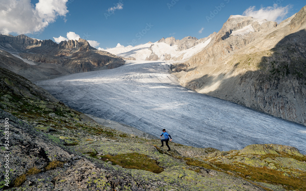 Running man in cross country trail run. Fit male runner sport training outdoors in beautiful mountain nature landscape with Rhone glacier and the mountains in the canton of Valais. Furka Pass. 