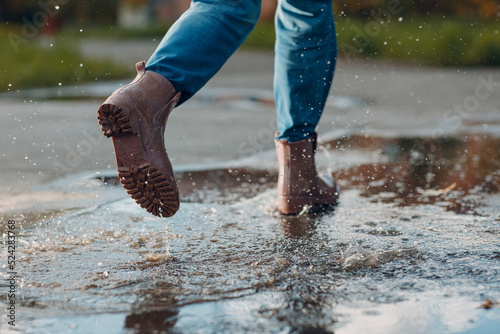 Photo Woman wearing rain rubber boots walking running and jumping into puddle with water splash and drops in autumn rain