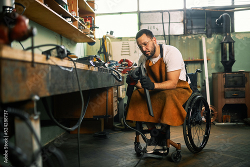 A manufacturer in a wheelchair grinds a metal part in his workshop.