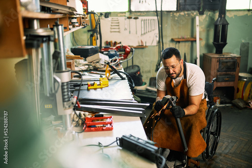 A manufacturer in a wheelchair is grinding metal bar in a workshop.