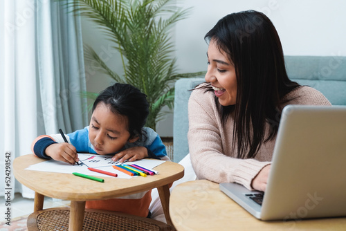Happy Asian mother working on computer laptop at home with her child - Focus on son face - Family concept
