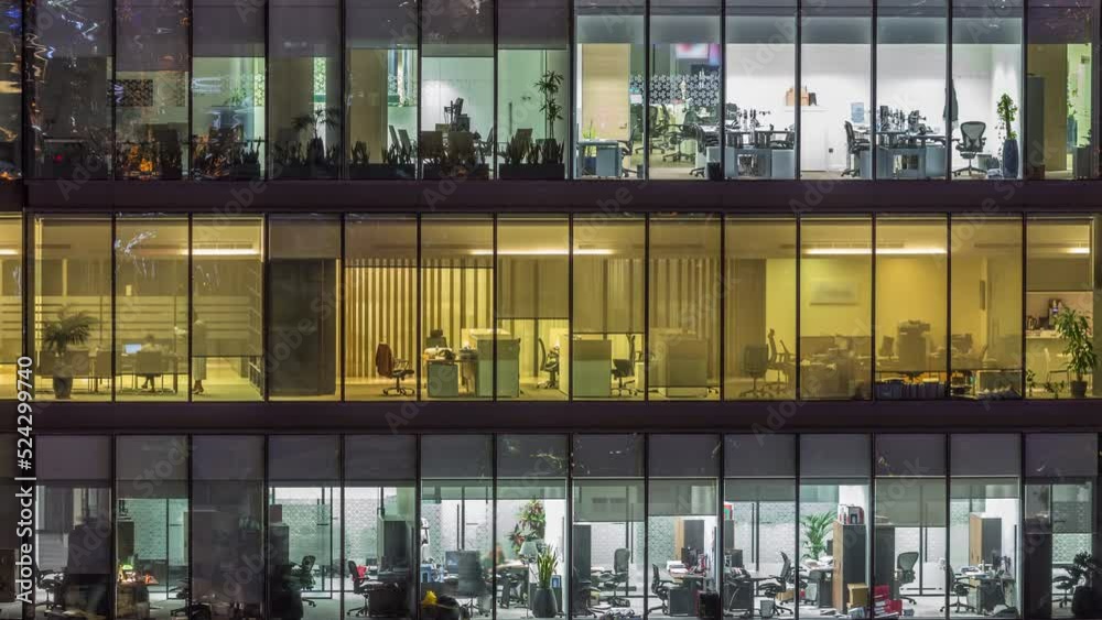Big glowing windows in modern office buildings timelapse at night, in rows of windows light shines. People working at tables inside