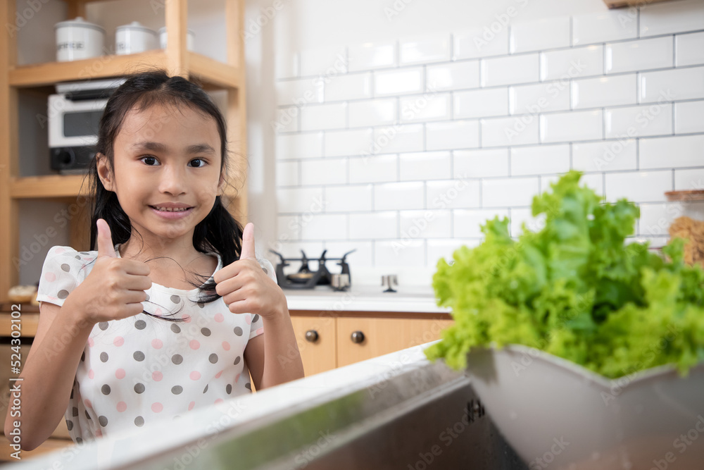 Little girl showing a thumb up sign after washing vegetable. Cute child helping her beautiful caring parents. Clean vegetable before eat and cooking Little girl showing a thumb up sign after washing vegetable. Cute child helping her beautiful caring parents. Clean vegetable before eat and cooking