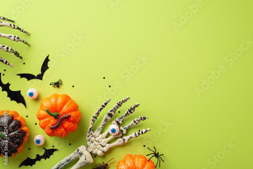 Halloween spooky decorations concept. Top view photo of skeleton hands holding eyeball pumpkins bat silhouettes insects spiders centipede and confetti on isolated light green background with copyspace