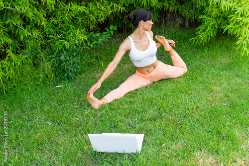 Woman doing Front splits with bind near laptop in park