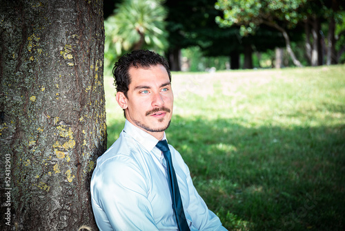 The beautiful businessman is working in a park. Portrait of young businessman with blue eyes.