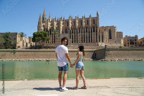 Couple in love gazing into each other's eyes with sunglasses and the famous cathedral of Palma de Mallorca in the background.