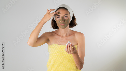 A woman in a towel after a shower applies a clay mask to her face - self-care at home