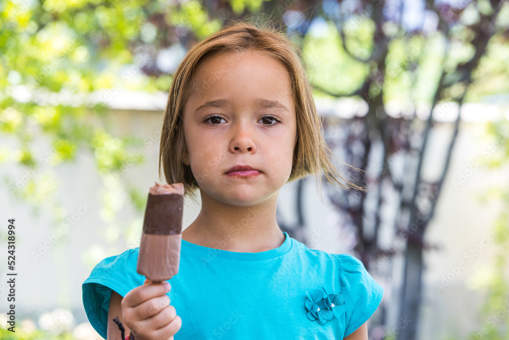 Unknown girl, wearing a green t-shirt, holding a milk chocolate ice cream, on the street, in summer, looking at the camera. Ice cream, popsicle, eating, sweet and summer concept. Unknown girl, wearing a green t-shirt, holding a milk chocolate ice cream, on the street, in summer, looking at the camera. Ice cream, popsicle, eating, sweet and summer concept.